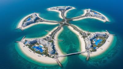Aerial drone view of Al Marjan Island, Ras Al Khaimah: a coral-reef-shaped archipelago of four interconnected man-made islands with white-sand beaches, low-rise resort hotels with bright blue swimming pools, and palm-lined access roads, surrounded by turquoise Arabian Gulf water
