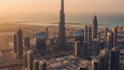 Sweeping aerial view of the Dubai skyline at golden hour with the Burj Khalifa rising above modern glass towers