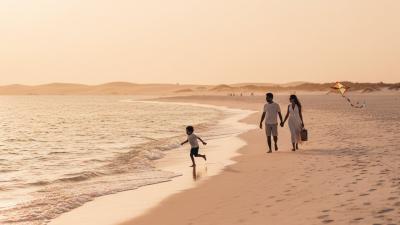 Silhouettes of an expat family of four walking on a Saadiyat-style white-sand UAE beach at golden hour, the youngest child running ahead toward the Arabian Gulf