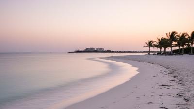 Wide ground-level view of a calm Saadiyat-style Abu Dhabi beach at early evening with white sand, gentle Arabian Gulf surf, and a coastal headland in the distance