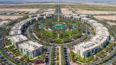 Aerial midday view of Dubai Silicon Oasis with low-rise tech-park buildings, tree-lined boulevards, and palm-lined parks