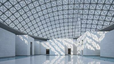 Interior of Louvre Abu Dhabi: dramatic 'rain of light' patterns filter through the geodesic silver dome, casting hundreds of overlapping star-shaped light shapes across pristine white limestone walls and a polished stone floor