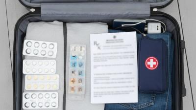 Open suitcase packed with medicine blister packs, a pill organizer and a folded prescription