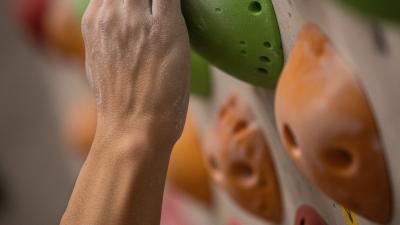Climber's chalked hand gripping a hold on a wall that shades from red through amber to green