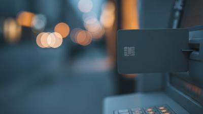 Blank dark payment card half-inserted into an ATM slot at dusk with street lights in soft focus