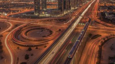 Aerial view of a UAE highway interchange at dusk with an elevated metro line and light trails