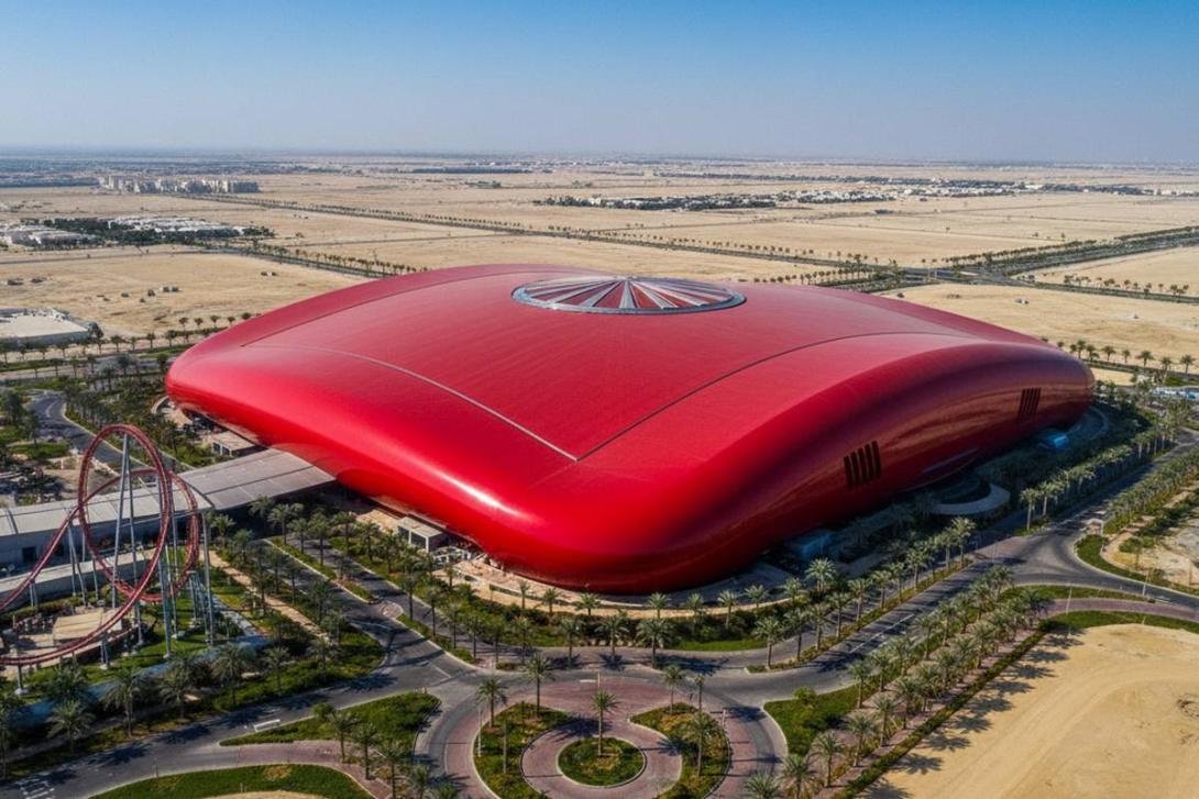 Aerial view of Ferrari World Abu Dhabi on Yas Island: the unmistakable bright red curving roof in the shape of a Ferrari GT car body dominates the frame, with manicured palm-lined paths and access roads spreading out across the desert sand and a roller-coaster track loop visible at the edge