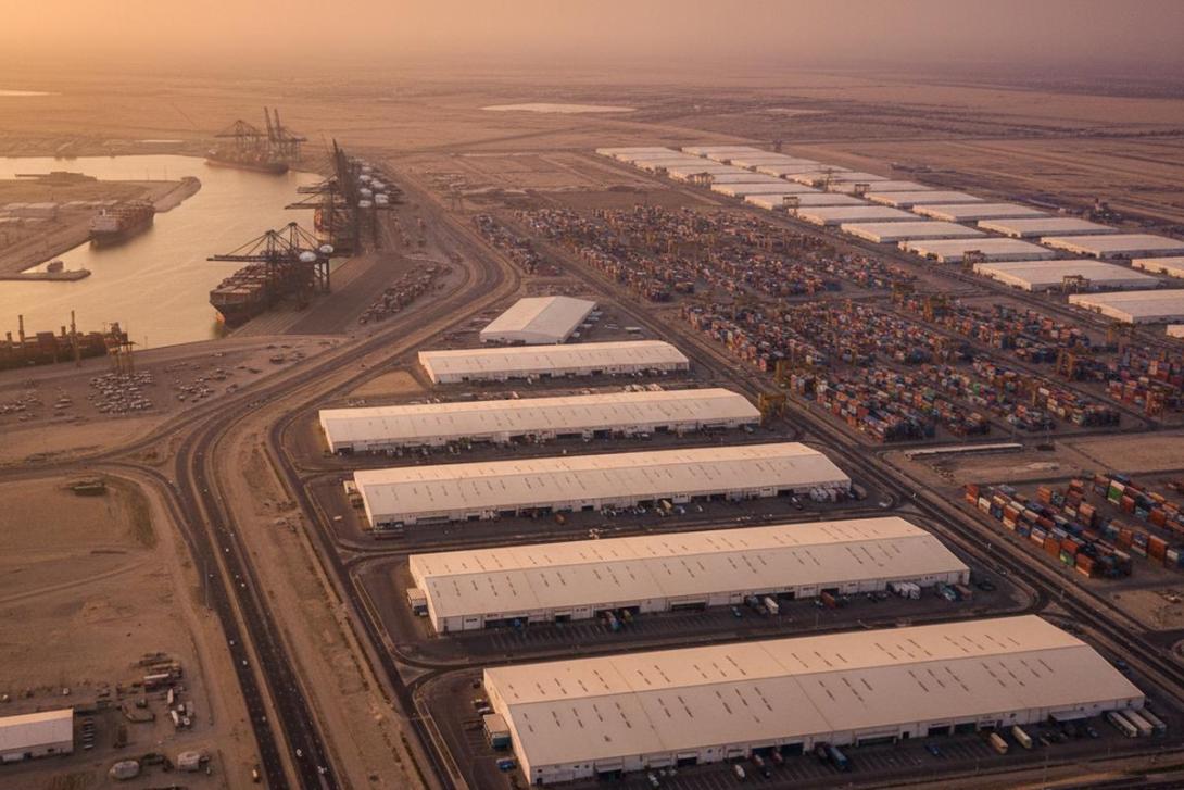 Aerial view of Jebel Ali Free Zone (JAFZA) at golden hour with vast warehouses, container stacks, and Jebel Ali Port cranes silhouetted against a warm sky