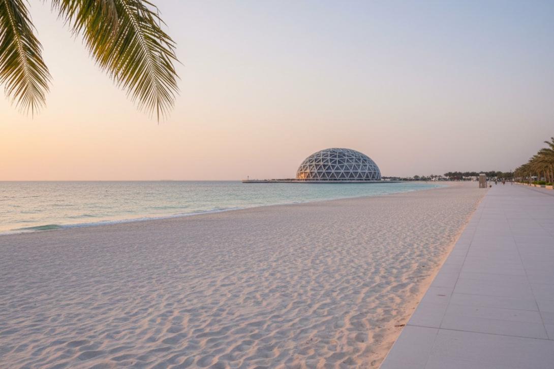 Late-afternoon view across Saadiyat Beach in Abu Dhabi: a paved promenade and palm fronds frame the right side of the image, with the silver geodesic dome of the Louvre Abu Dhabi visible low on the horizon across the white sand and turquoise Gulf water