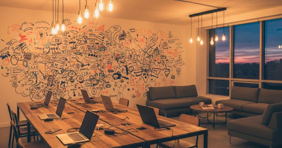 Modern startup coworking space interior at evening with shared work tables, laptops, and warm Edison-bulb pendant lighting