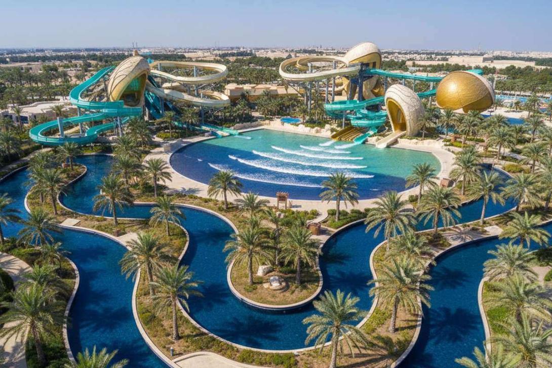 Aerial view of Yas Waterworld Abu Dhabi: vibrant blue and turquoise lazy-river channels and pools wind between curving fibreglass slide structures themed in pearl-diving aesthetics, with a central wave pool and palms throughout