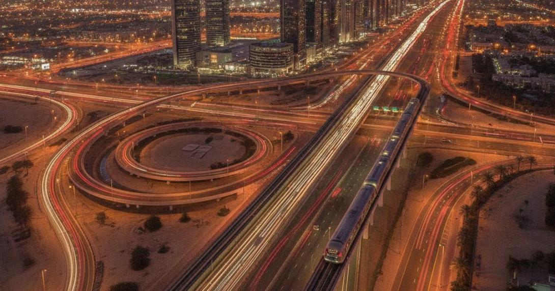 Aerial view of a UAE highway interchange at dusk with an elevated metro line and light trails